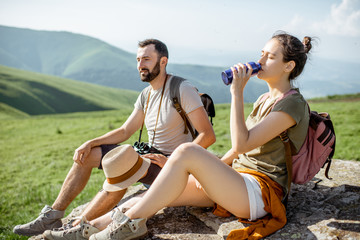 Fototapeta premium Young couple drinking water while resting on the rock during the travel in the mountains