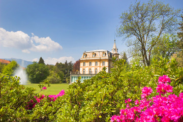 spring landscape with pink flowers and beautiful villa house with fountain in bright day blue sky background.