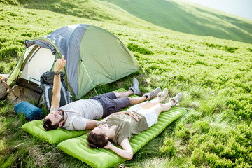 Young and cheerful couple lying on the mattress at the campsite, enjoying summer time while...