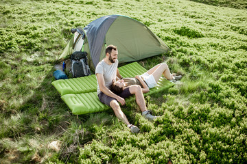 Young lovely couple sitting together on the mattress at the campsite, enjoying summer time while...