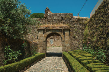 Fototapeta na wymiar Pathway going toward gateway in stone wall with garden