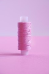 Close up one spool of sewing thread lilac (pink, violet, crimson) on a pink paper backgroun, copy...