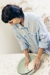 Obraz na płótnie Canvas Middle-aged brunette woman kneading making dough for dumplings in blue bowl.