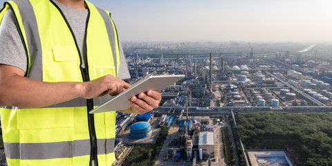 worker working on pad with oil and gas refinery background,Smart factory concept.