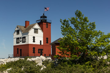 A red & white lighthouse on a rocky beach.  Round Island Lighthouse, Hiawatha National Forest, MI, USA.