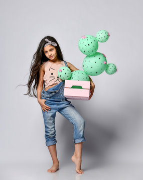 Young brunette girl hold cactus balloon in pastel pink wooden box. Flowers are made of balloons with pink flowers and painted spines. Creative idea minimal concept on gray background