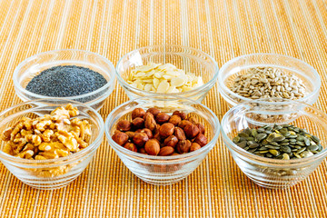 Small glass bowls with poppy seeds, sliced almonds, sunflower seeds, walnuts, hazelnuts, and pumpkin seeds.