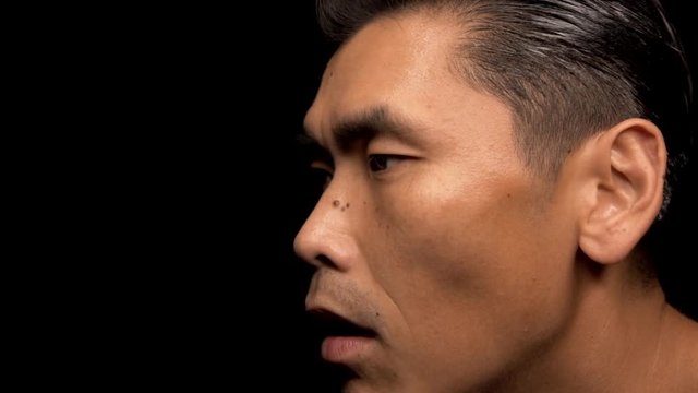This slow motion video shows the profile of an asian man as he is coughing and choking with black background.