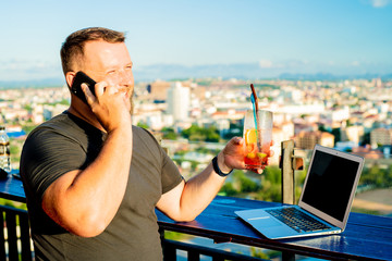 man talking on the phone and working on a computer in a cafe with a beautiful view