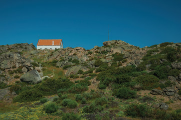 House on top of hilly landscape with bushes and rocks