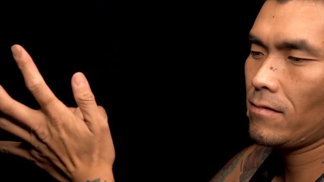 This video shows a tattooed asian man smashing a can and tosses it away against a black background.