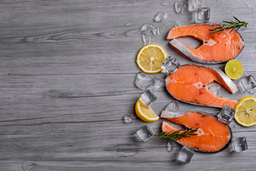 Salmon steaks on ice with lemon and rosemary on dark wooden table top view. Fish food concept. Copy space