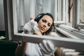 Beautiful and diligent middle age handy woman renovating her old home or apartment. She is holding professional paintbrush and painting windows. Do it yourself housework concept.