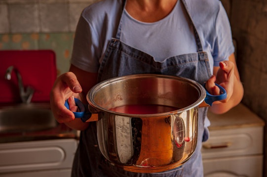 woman cook in an apron prepares tomatoes in a saucepan, rubs through a sieve and prepares tomato juice. Female hands closeup.