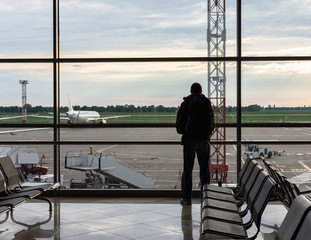 Man with a backpack on his shoulders looks out the window at the planes at the airport, air tourism