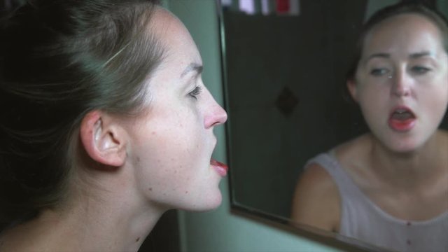 This slow motion video shows a sick and troubled young woman looking into a dirty bathroom mirror and spitting blood.