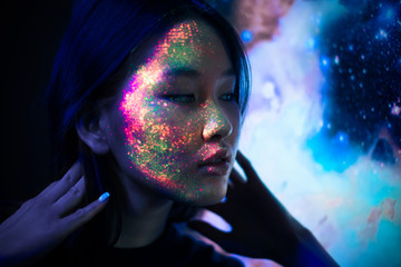 Beautiful young woman dancing and making party with fluorescent painting on her face. Neon facial...