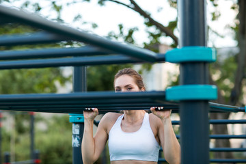 Obraz premium Young woman is training on the outdoor playground and pulls up on the horizontal bar. Crossfit and fitness workout outdoors.