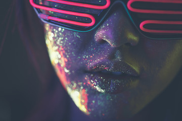 Beautiful young woman dancing and making party with fluorescent painting on her face. Neon facial...