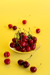 Freshly picked cherries in a glass bowl. Bright yellow background, water drops, high resolution