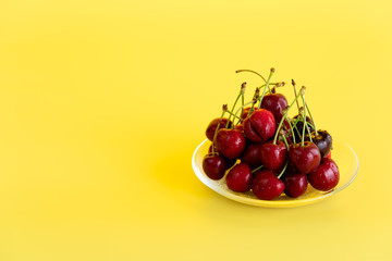 Freshly picked cherries in a glass bowl. Bright yellow background, water drops, high resolution, negative space