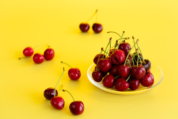 Freshly picked cherries in a glass bowl. Bright yellow background, water drops, high resolution