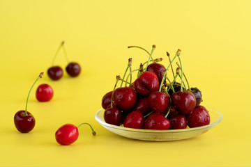 Freshly picked cherries in a glass bowl. Bright yellow background, water drops, high resolution