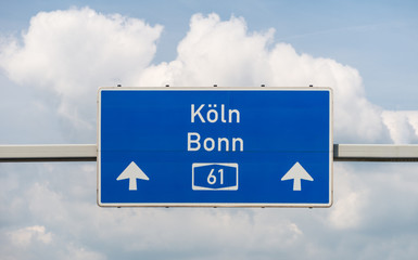 A large road sign above the German highway number 61, against the sky with clouds.