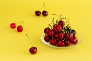 Freshly picked cherries in a glass bowl. Bright yellow background, water drops, high resolution