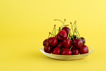 Freshly picked cherries in a glass bowl. Bright yellow background, water drops, high resolution, negative space