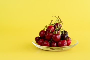 Freshly picked cherries in a glass bowl. Bright yellow background, high resolution, negative space