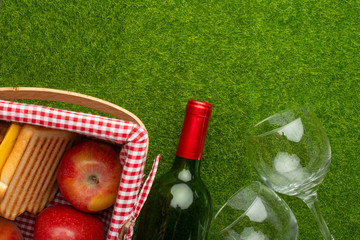 Naklejka premium Picnic on green grass with a bottle of wine and two glasses with a picnic basket in which the senviches and fruits. background of rest and relaxation. Summer relaxation and mood.