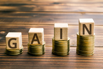 inscription gain wooden cubes with letters, money piles of coins,  wooden background