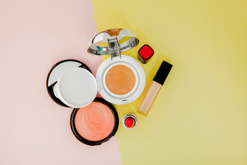 Make up products spilling on to a bright yellow and pink background with copy space