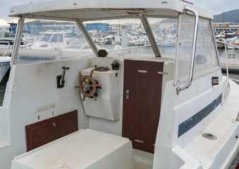 View on the cockpit of the boat, old steering wheel. Wheelhouse of the small motorboat. Wood steering wheel,  gear lever, compass. Boat service in the port, preparing to sail.  © Olga