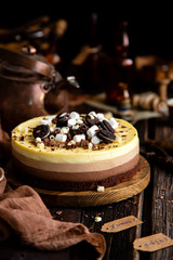 Fototapeta na wymiar Beautiful still life with homemade delicious three chocolates cheese cake on wooden stand on rustic table