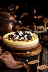 Beautiful still life with homemade delicious three chocolates cheese cake on wooden stand on rustic table