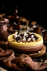 Beautiful still life with homemade delicious three chocolates cheese cake on wooden stand on rustic table