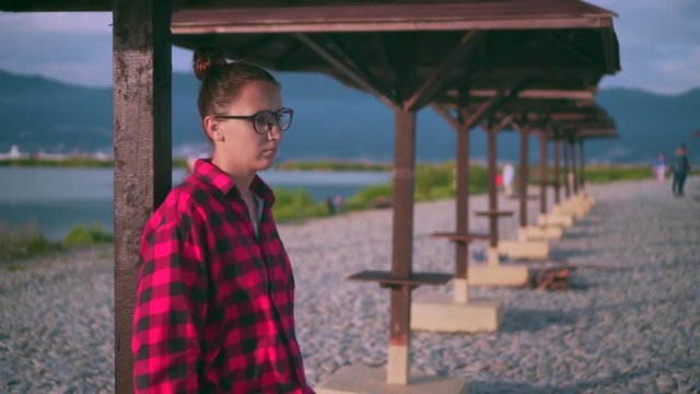 Beautiful young girl with glasses and a red checkered shirt in and relaxes. In the background are many wooden parasols on the beach.
