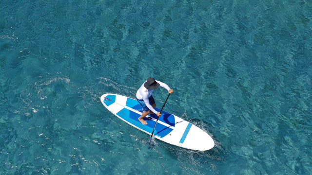 Aerial photo of unidentified fit man practising SUP or Stand Up Paddle in tropical exotic destination island with turquoise sea