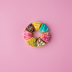 Donut shape made of cut donut slices on pink background.