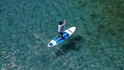 Aerial photo of unidentified fit man practising SUP or Stand Up Paddle in tropical exotic destination island with turquoise sea