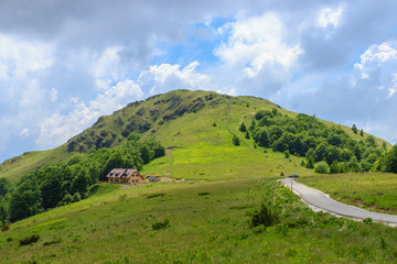 Picturesque view of the green hill, blue sky, road and the cottage