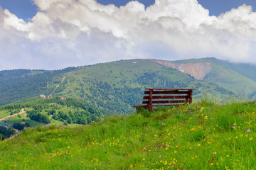 Wooden bench at the top of the hill and the beautiful view of the mountains