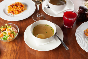 Hot autumn chicken soup as a part of set menu, placed on a wooden table with other males on background