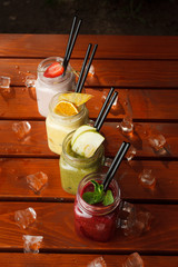 Variety of smoothies on a summer terrace wooden table with ice cubes on it: strawberry, apple green, citrus and berries smoothies