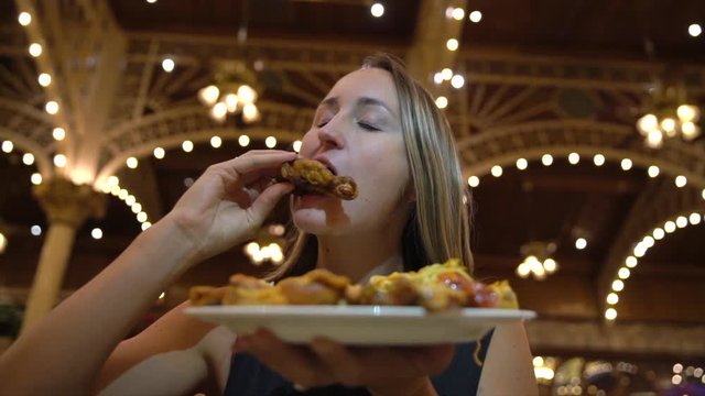 This slow motion video shows a young caucasian woman devouring a plate full of chicken wings