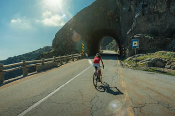 Road passing through rocky terrain with cyclist and tunnel