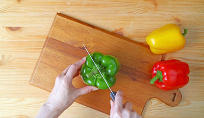 Woman's hand cutting a green bell pepper on wooden cutting board