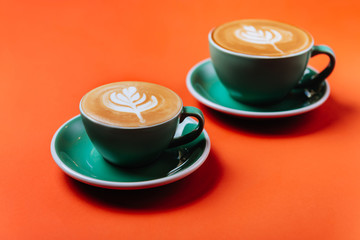 Cyan cappuccino coffee cups over orange background. Top view flat lay with copy space